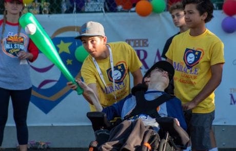 A boy in a wheelchair is holding a baseball bat.