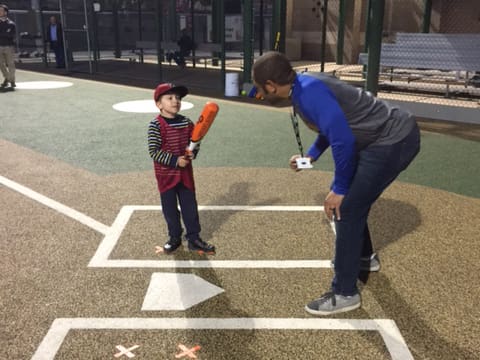 A man teaches a young boy how to hit a baseball.