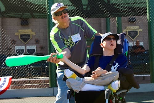 A man in a wheelchair is playing baseball with a boy in a wheelchair.
