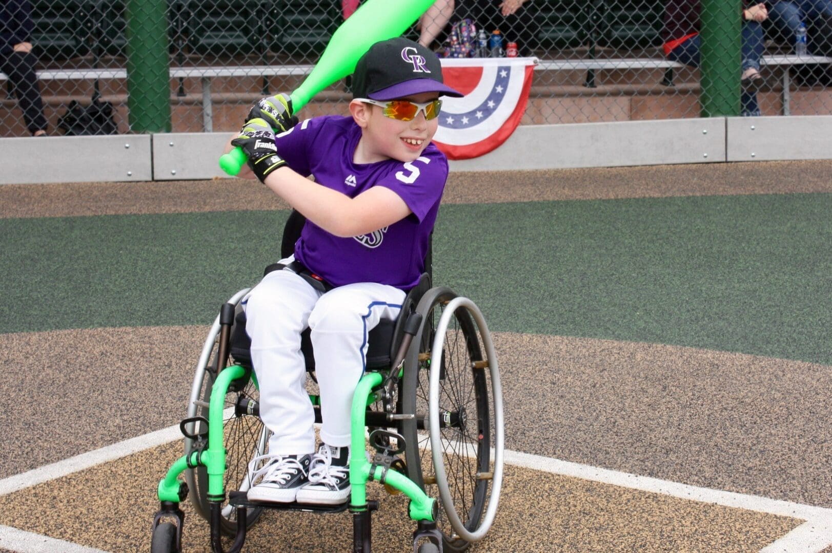 A boy in a wheelchair swinging a bat at a baseball game.