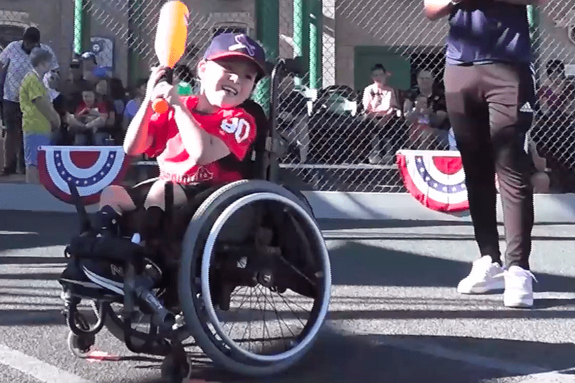 A boy in a wheelchair playing baseball with a bat.