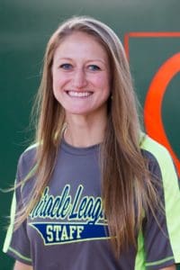 A female softball player is smiling in front of a green wall.