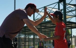 A man is giving a boy a high five on a baseball field.
