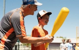 A man is holding a yellow baseball bat with a young boy.