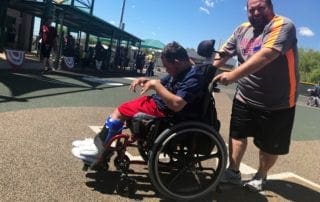A man in a wheelchair is pushing a boy to a baseball field.