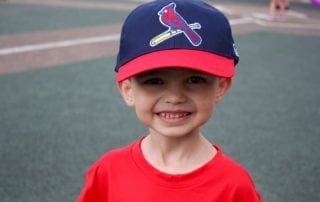 A young boy wearing a st louis cardinals hat.