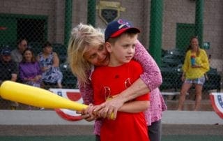 A woman hugging a boy with a baseball bat.