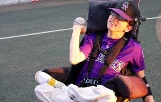 A young boy in a wheelchair sitting on a baseball field.