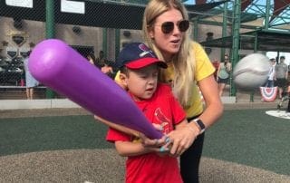 A woman is holding a purple baseball bat with a young boy.