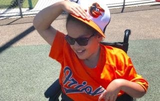 A young boy in a wheelchair wearing an orioles hat.