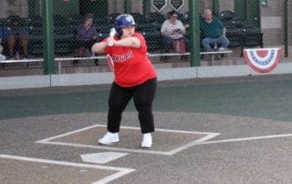 A woman swinging a baseball bat in front of a crowd.