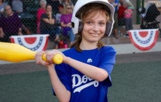 A young girl holding a bat in front of a crowd.