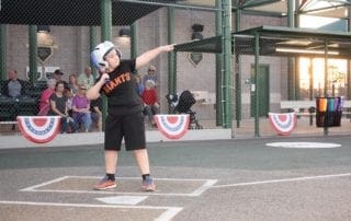 A young boy swinging a baseball bat in front of a crowd.