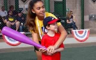 A woman holding a purple baseball bat with a young boy.
