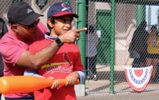 A man pointing to a young boy with a baseball bat.