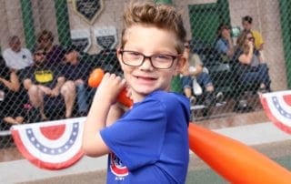 A young boy with glasses holding a baseball bat.