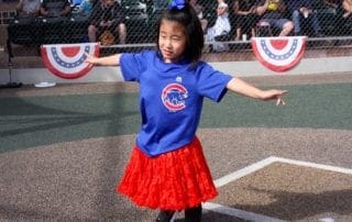 A girl in a red skirt is standing on a baseball field.