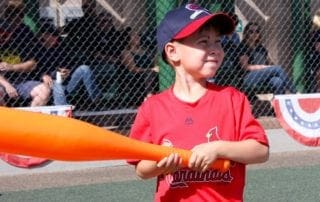 A young boy holding an orange baseball bat.