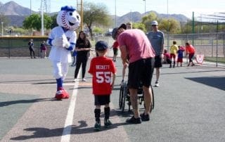 A boy in a wheelchair is being helped by a baseball mascot.
