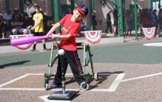 A boy in a wheelchair swinging a baseball bat.