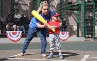 A woman teaches a young boy how to hit a baseball.