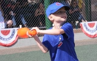 A young boy swinging a bat at an orange ball.