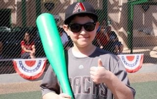 A boy holding a baseball bat and giving a thumbs up.