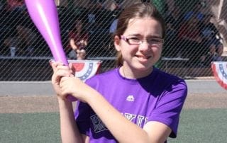 A young girl holding a purple baseball bat.