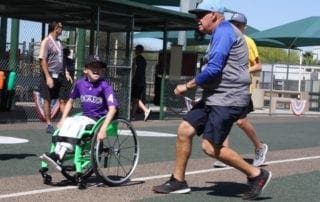 A man in a wheelchair pushing a boy in a wheelchair.