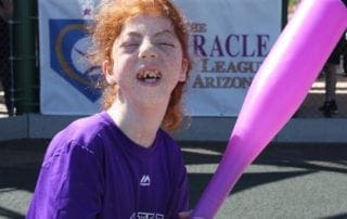 A girl with a purple shirt holding a pink bat.