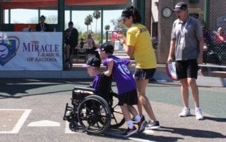 A woman in a purple shirt is helping a boy in a wheelchair on a baseball field.