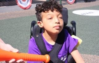A young boy in a wheelchair holding a baseball bat.