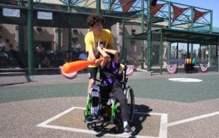 A boy in a wheelchair playing baseball with an orange ball.