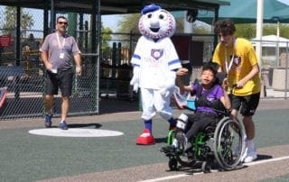 A boy in a wheelchair is being helped by a mascot.