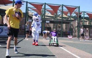 A man in a wheelchair and a mascot on a tennis court.
