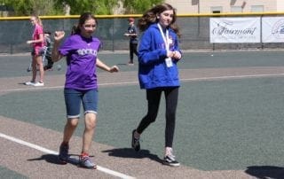 A group of girls are running on a baseball field.