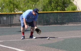 A man bending down to catch a baseball.