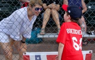 A woman talking to a young boy at a baseball game.