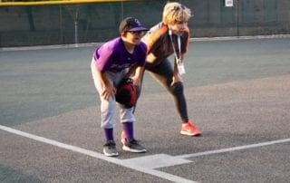 A girl wearing a purple baseball catcher's mitt and a boy wearing a purple baseball catcher's mitt.