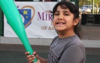 A young girl holding a green baseball bat.