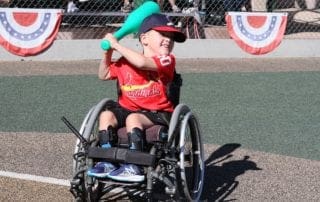 A boy in a wheelchair swinging a bat.