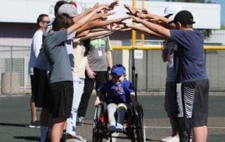 A group of people huddle around a boy in a wheelchair.