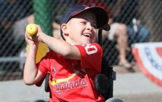 A young boy in a wheelchair swinging a baseball.