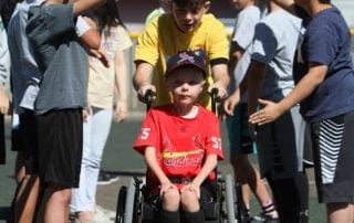 A young boy in a wheelchair is surrounded by people.