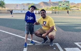 A man posing with a young boy on a baseball field.