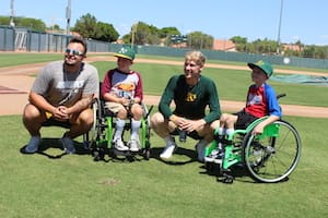 Three boys in wheelchairs posing for a photo on a baseball field.