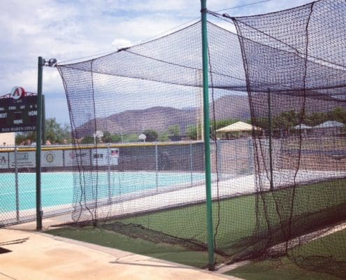 A baseball batting cage with a pool in the background.