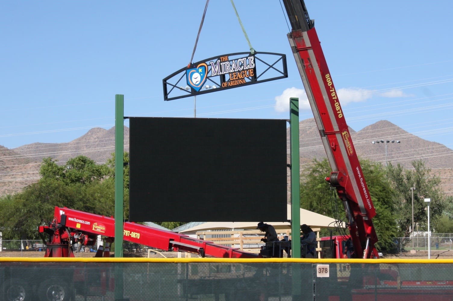 A crane lifts a large sign onto a baseball field.
