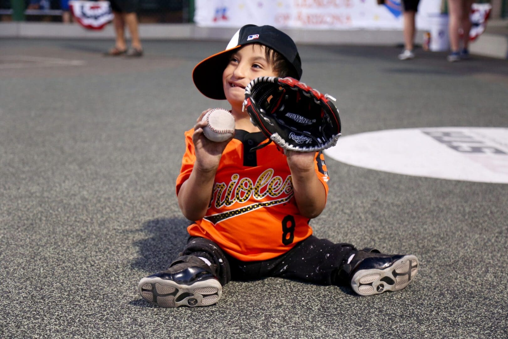 A young boy sitting on the ground holding a baseball.