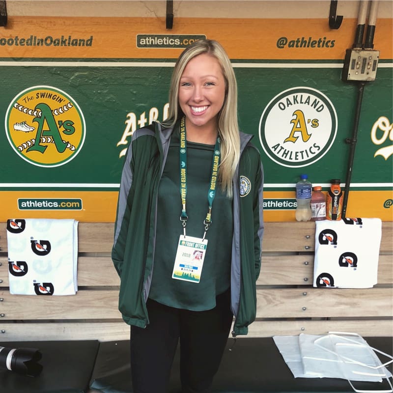 A woman in a green jacket standing in a dugout.